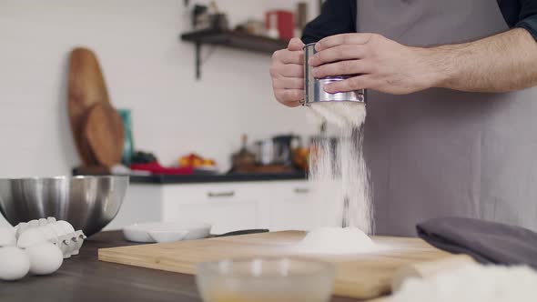 The chef in an apron kneads the dough. Close-up of a cook's hand. Flour is scattered on the table