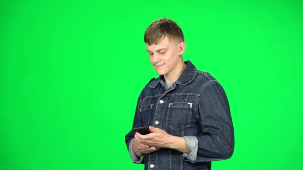 Smiling Man Goes and Texting with Smartphone on Green Screen at Studio, Slow Motion