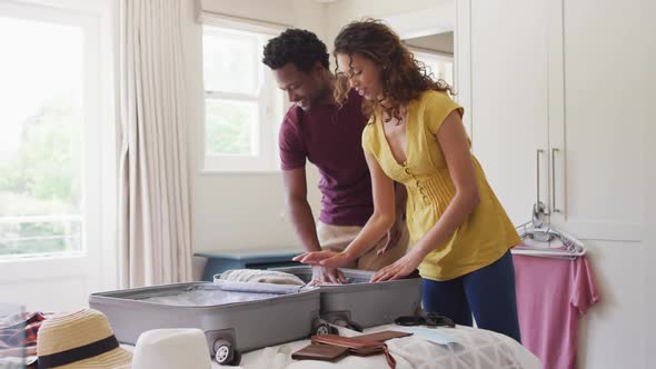 Happy biracial couple packing clothes into suitcase together, preparing for travel