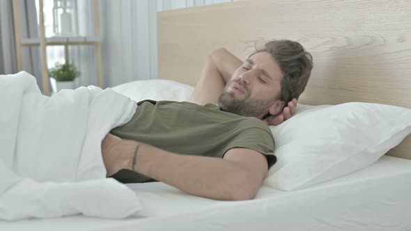 Tired Young Man Having Back Pain While Sleeping in Bed