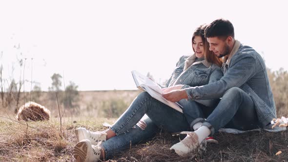 Attractive Young Man Is Hugging His Girlfriend Reading a Book in the Field