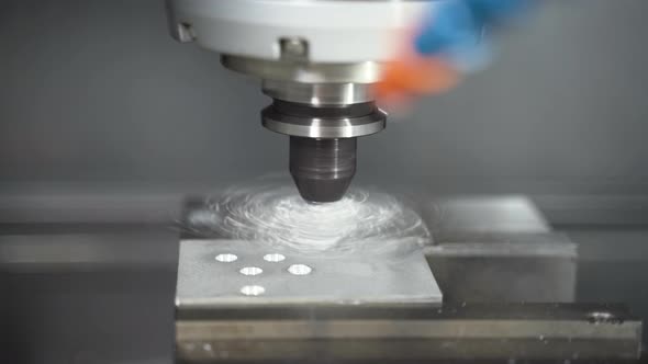CNC machine drilling screw holes in a metal plate in a vice, close up.