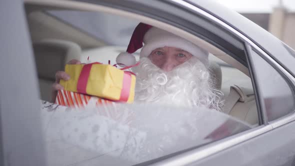 Old Santa Claus Opening Car Window and Winking, Bearded Santa Sitting in the Car on Back Seat 