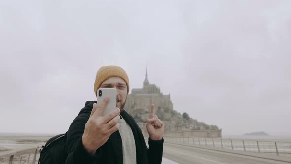 Happy Young Smiling Caucasian Blogger Man Making Video Call Using Smartphone at Mont Saint Michel