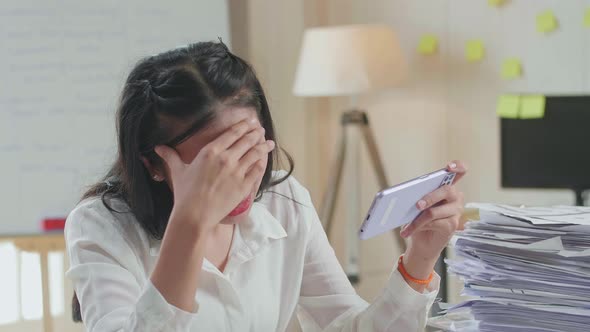 Close Up Of Asian Woman Being Upset Losing Game On Smartphone After Working With Documents