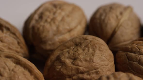 Cinematic, rotating shot of walnuts in their shells on a white surface 