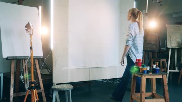 Blond Woman Comes to a Canvas and Touches It