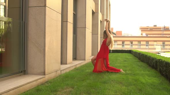 Beautiful Young Girl Dancing on Green Grass Against the Background of a Modern City