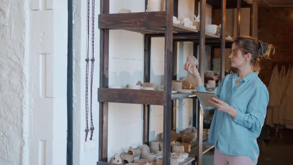 Young Lady Writing Inventory Information About Ceramic Artworks in Pottery Studio