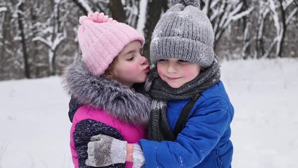 Beautiful Little Girl Kisses a Boy on the Street in Winter in a Snowcovered Forest