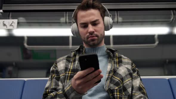 Handheld Focused Man Rides the Subway Listens to Music with Wireless Headphones and Uses a