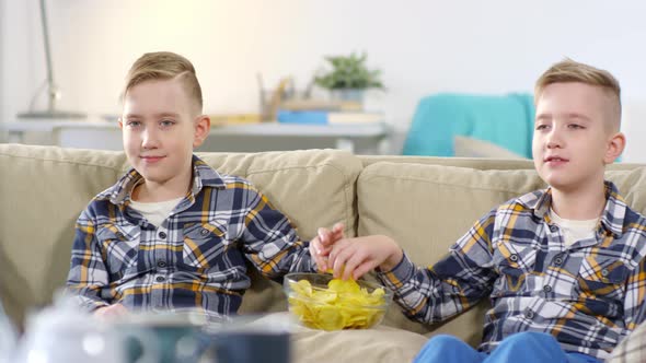 Caucasian Twins Grabbing Same Crisp from Bowl