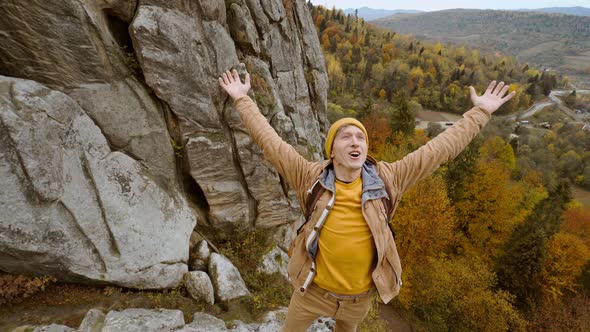 Happy Man Hiker with Backpack Relaxing on Top of a Cliff and Enjoying the View of Valley Tustan