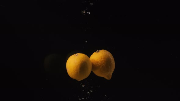 Lemons Falling Into Water with Bubbles on Black Background. Сitrus Falling Into Water. Slow Motion