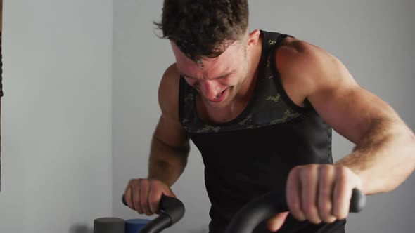 Fit sweaty caucasian man exercising on training bike inside gym