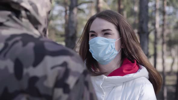 Portrait of Young Caucasian Woman in Face Mask Talking To Unrecognizable Man and Coughing. Brunette