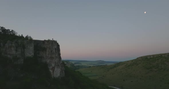 silhuette of a single man standing on top of a cliff with moon on background