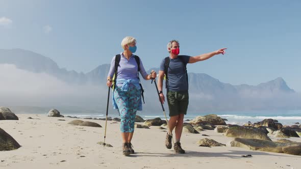 Senior hiker couple wearing face masks with backpacks and hiking poles pointing towards a direction 