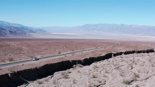 White Tesla car driving along desert road by the cliff. Mountains in the background. Hot sunny day i