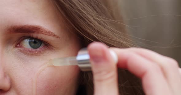 close-up a drop of serum falls on the skin the face of a fair-haired girl, a green eye clips