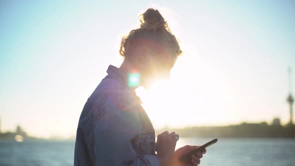 Slowmotion Side View of Charming Female Photographer with Blond Hair Standing on Pier Near Sea As