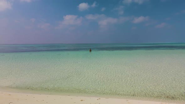 A man stands in turquoise water against a stormy sky. The camera moves smoothly