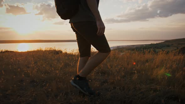 Male Photographer with Backpack and Tripod in It is Walking Along Meadow on Plato of a Mountain and