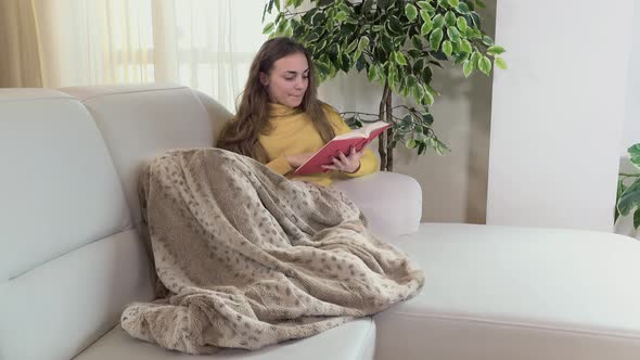 Young Woman Enjoys Reading the Book on the Sofa