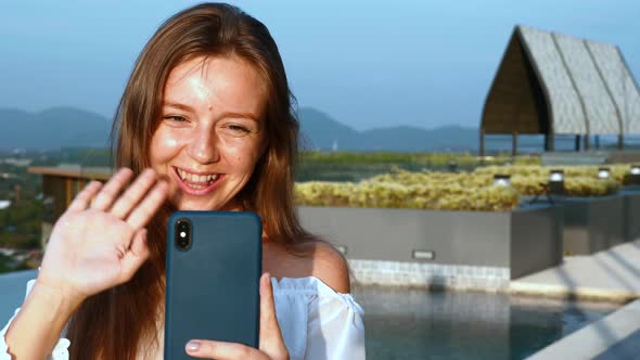 Young Smiling Woman with Smartphone Making Video Call on Rooftop of Hotel