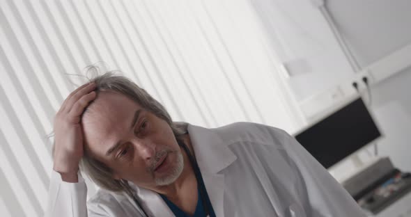 Senior Male Doctor Looking Tired Standing in Hospital Ward