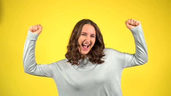 Attractive Curly Young Woman Raising Arms Up Isolated on Yellow