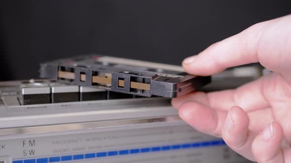 Male Hand Takes an an Old Audio Cassette Lying on Buttons of Retro Tape Recorder