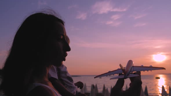 Happy Mother with Little Son Playing with Toy Plane at Sunset, Attractive Mother and Child Hugging