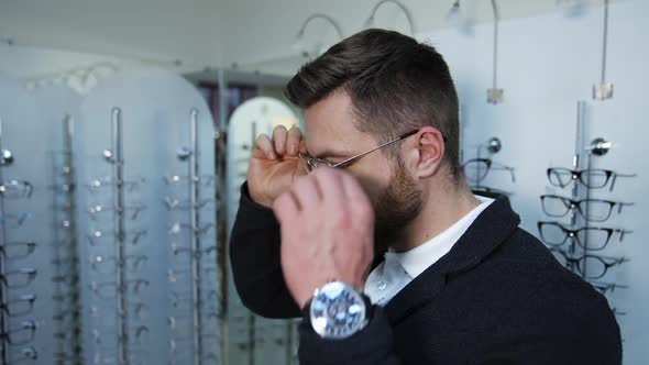 Man choosing glasses at optical store. Young man in optical store trying eyeglasses