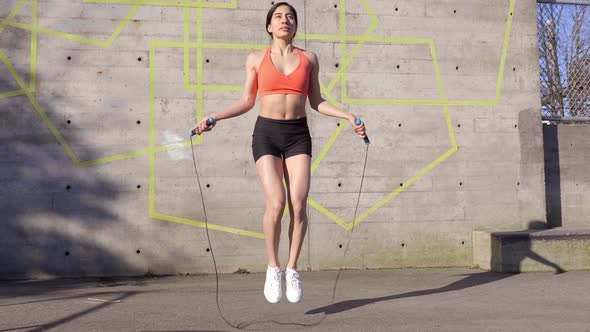 Young Latina Woman using jump rope by concrete wall, Wide Shot