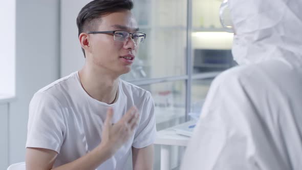 Infected Asian Man Talking to Doctor in Disposable Coveralls alt
