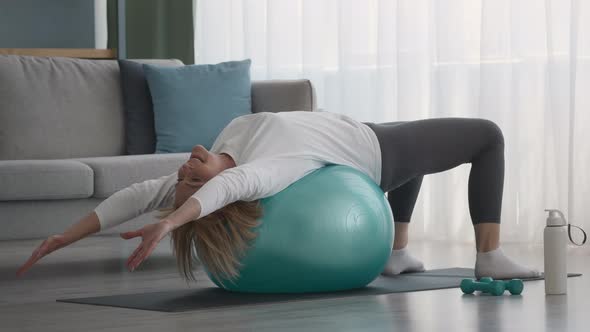 Older Woman Doing Pilates Stretching Exercise Lying On Fitball Indoor