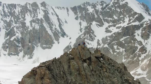 Four Climbers on Peak of Rock. Snow-Capped Mountains. Aerial View