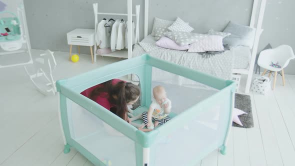 Loving Mother Playing with Infant Girl in Playpen