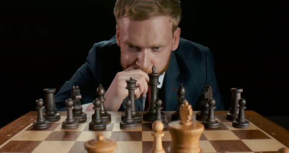 Portrait of Pensive Caucasian Businessman Playing Chess at Table Isolated on Black Background