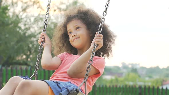 Little Curly-Haired Girl Swinging in Back Yard and Dreaming About Happy Future