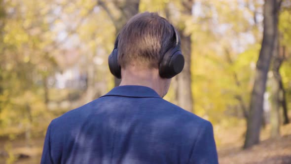 A Middleaged Handsome Caucasian Man Listens to Music with a Headset and Walks in a Park in Fall