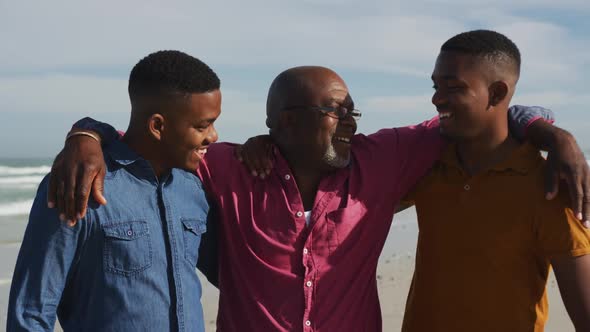 African american senior father and twin teenage sons walking on a beach and talking