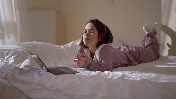 Relaxed Little Woman Singing Listening to Music in Headphones Lying on Bed at Home