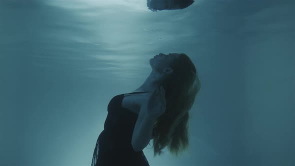 Woman with Red Hair Poring in a Black Dress Underwater