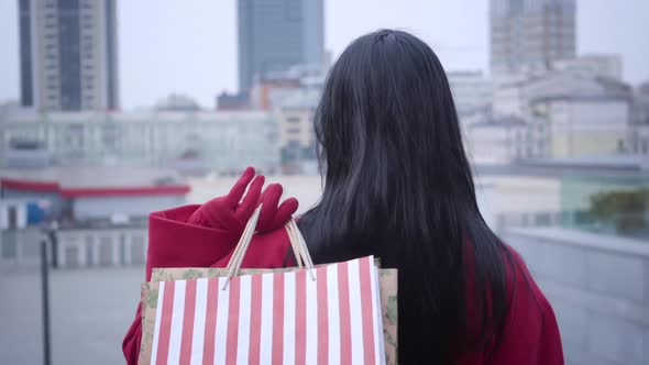 Back View of Stylish Lady with Black Hair Standing with Shopping Bags, Turning To Camera and Winking