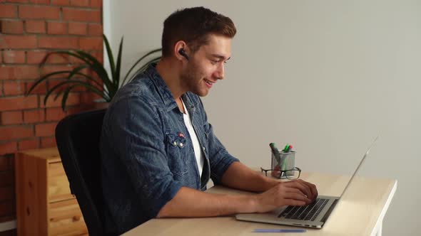 Side View of Cheerful Young Man Student Wearing Headphones with Microphone Communicating Via Video