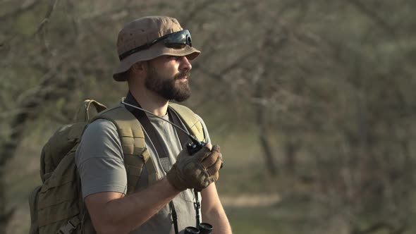 Outdoor Shot of Seriouslooking Man Hunter in Military Clothes with Binoculars and Backpack Talking