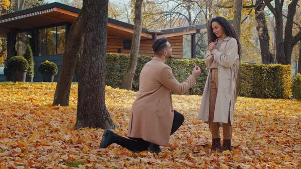 Young Guy Kneels Makes Romantic Marriage Proposal to Girlfriend Smiling Happily Man Puts Ring on