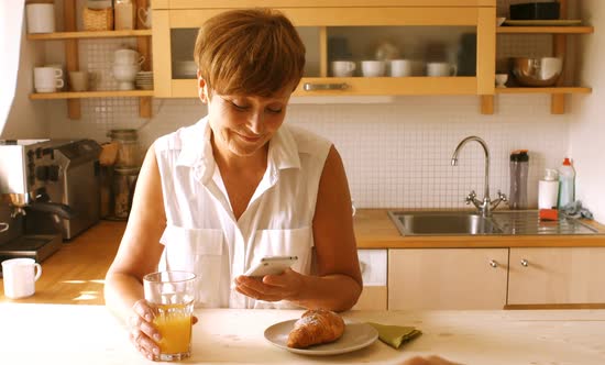 Senior woman using mobile phone while having breakfast in kitchen